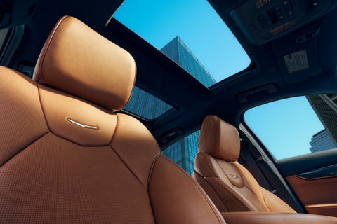 View from inside a car with a sunroof, showing brown leather seats and city buildings against a blue sky.