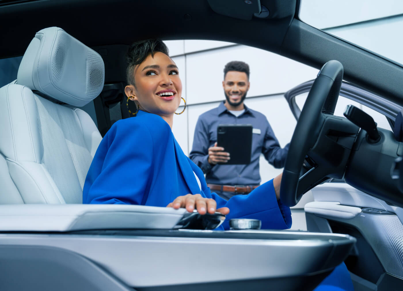Customer sitting inside a white Cadillac cabin talking with a service advisor holding a tablet.