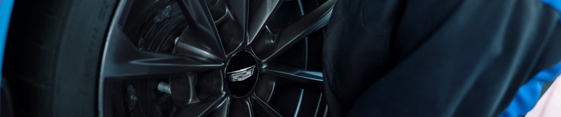 Close-up view of a technician inspecting the dark alloy wheel of a blue Cadillac.