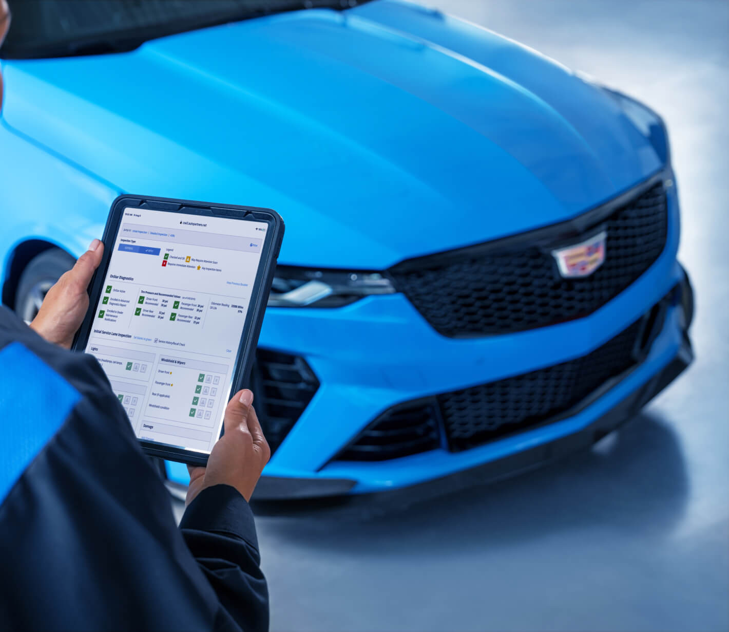 Front view of a technician holding a diagnostic tablet before a blue Cadillac CT4-V in a service bay.