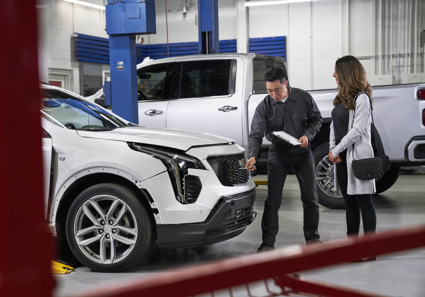 Front view of a service advisor reviewing a white 2026 Cadillac XT4 with a female customer in a service bay.