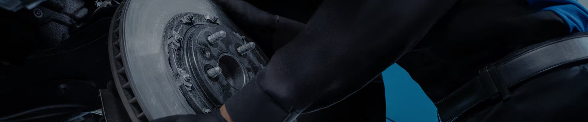 Close-up view of a technician wearing black gloves installing a brake rotor on a vehicle in a service bay.