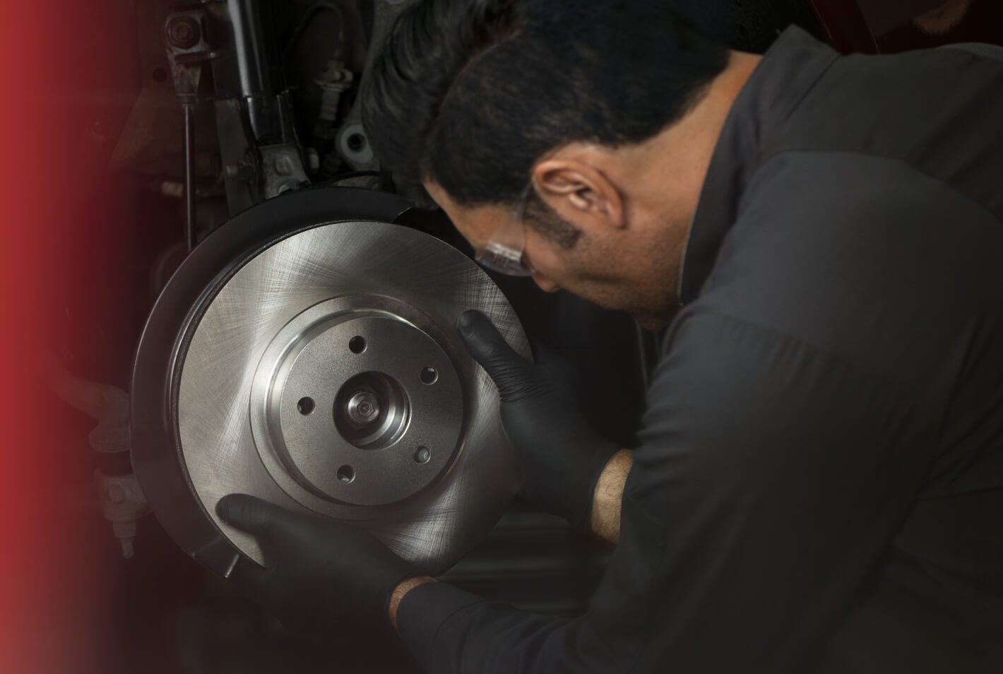 Close-up view of a male technician wearing safety glasses holding a new brake rotor in a service bay.