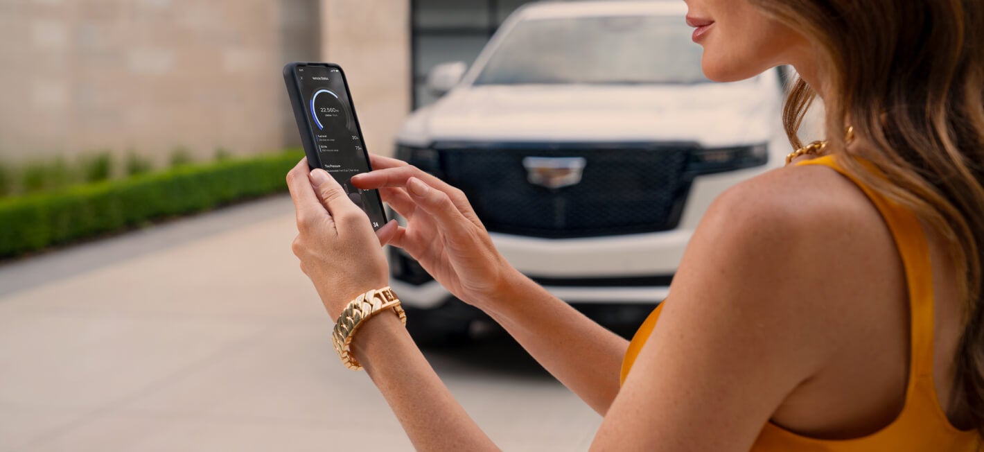 Close-up view of a woman using a smartphone vehicle app in front of a 2026 Cadillac Escalade.