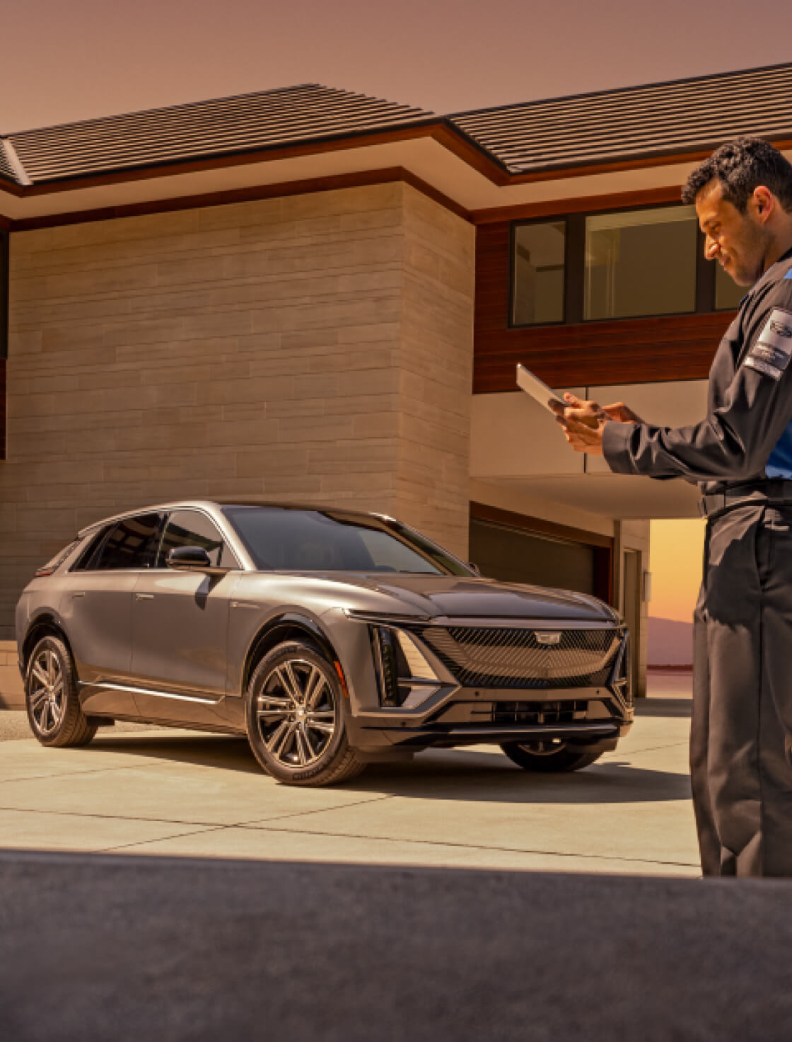 Side profile view of a technician using a digital tablet next to a 2026 Cadillac LYRIQ parked outside a modern home.