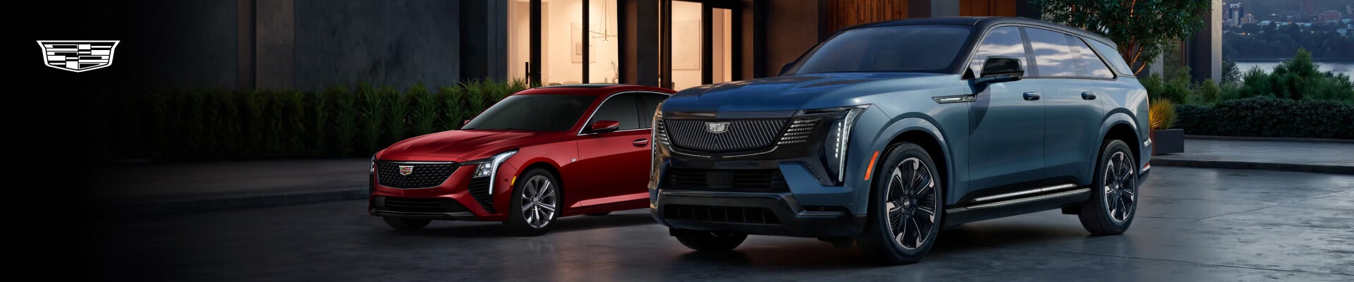 A red Cadillac CT5 and a blue Cadillac Escalade IQ parked in the driveway of an upscale home.