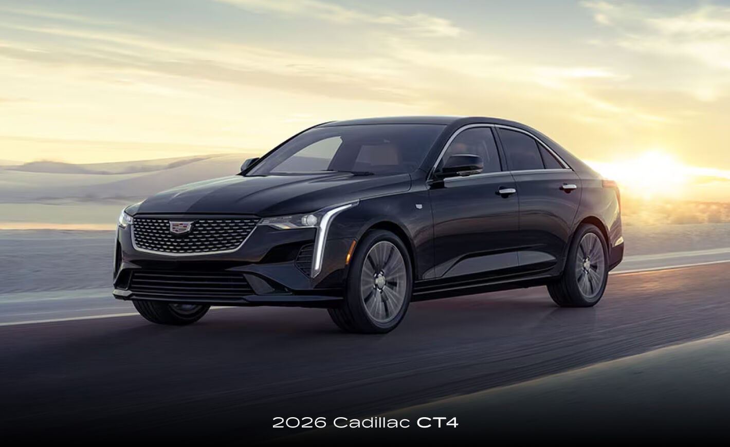 Front exterior action shot of a 2026 Cadillac CT4 driving down a remote highway at golden hour.