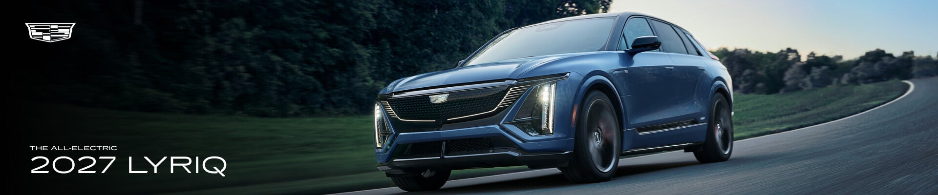 External front low angle action shot of a blue 2027 Cadillac LYRIQ driving down a country road.