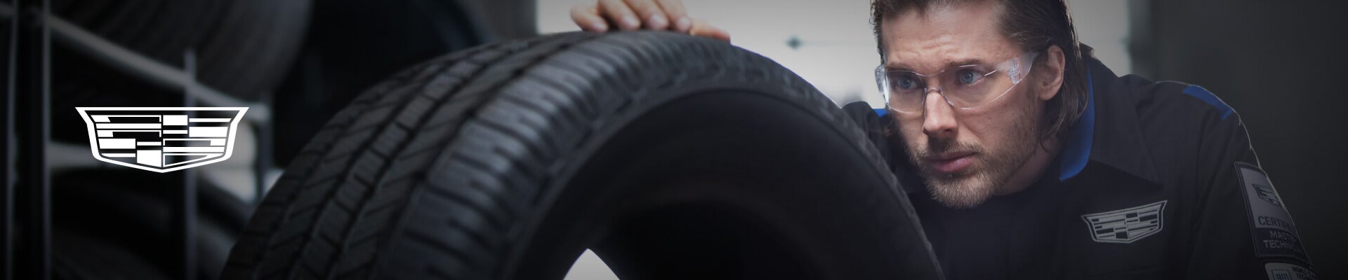 A Cadillac Service Technician closely inspects a new tire in a bright, clean service center.