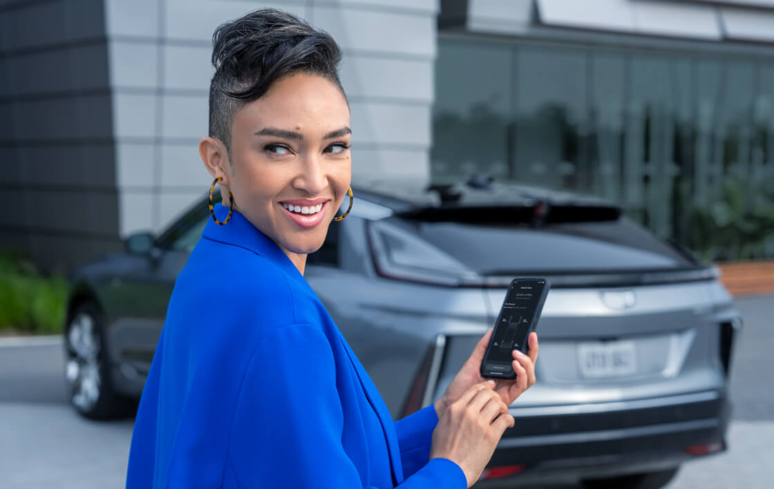 A woman looks over her shoulder and smiles as she holds her phone near her Cadillac.
