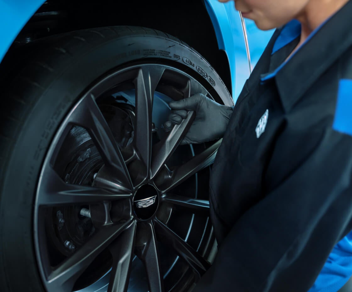 Close-up of two gloved hands inspecting the wheel of a blue Cadillac.