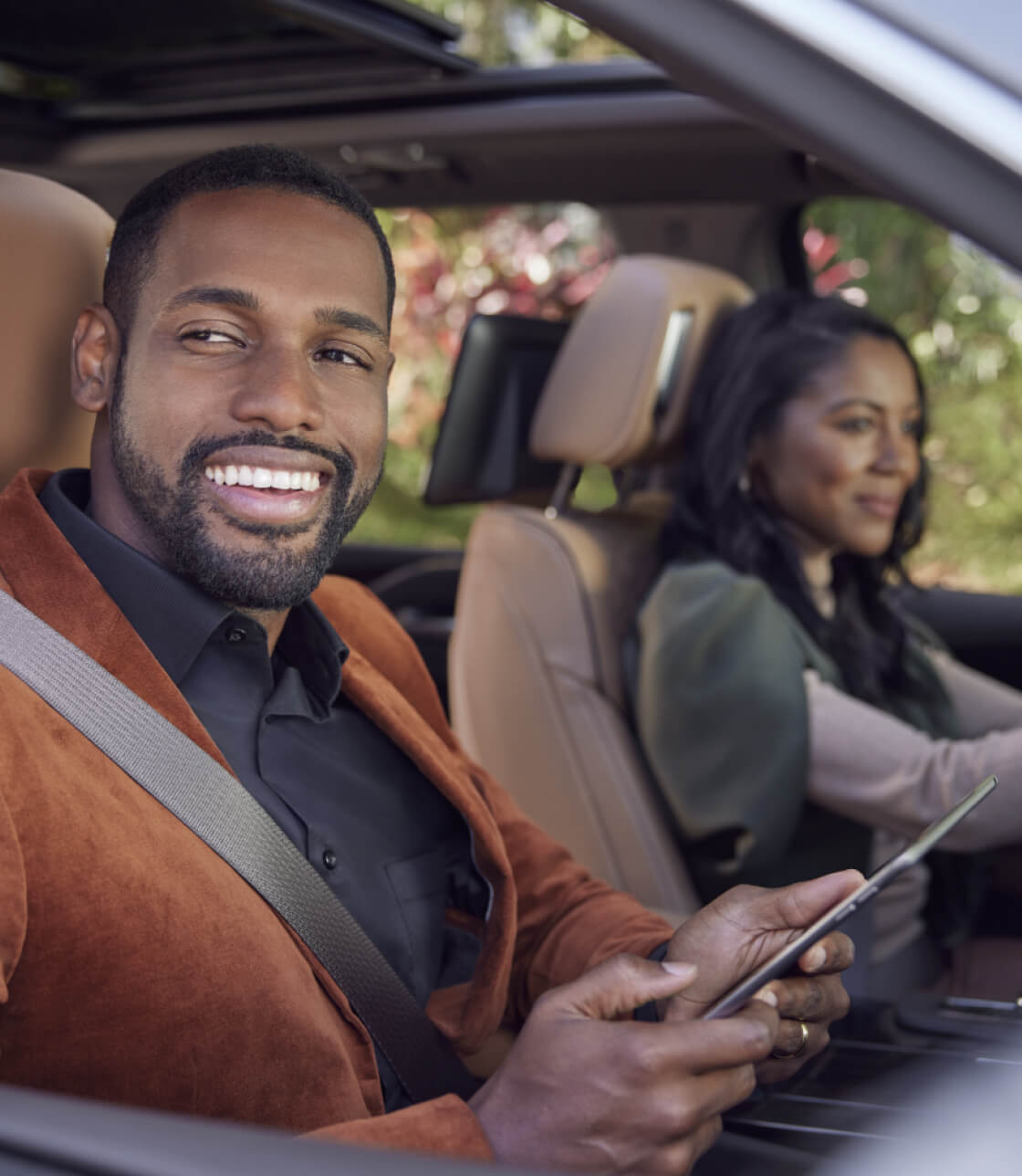 A couple sits in the front seats of a Cadillac and smiles while looking out the window.