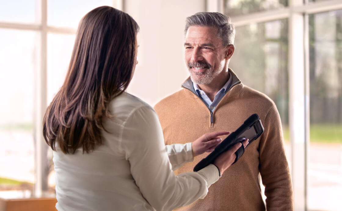 A man smiles as a Cadillac Sales Associate points him to her tablet.