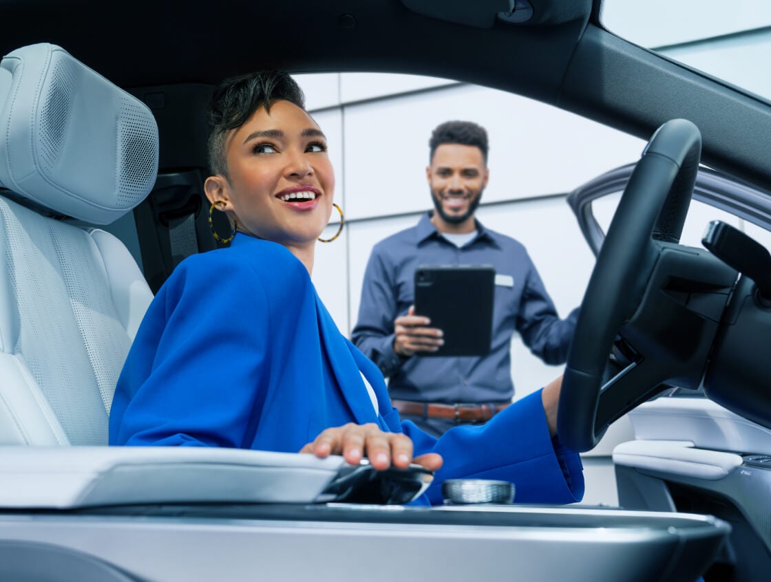 A woman smiles in her Cadillac as a Service Manager smiles outside her open car door.